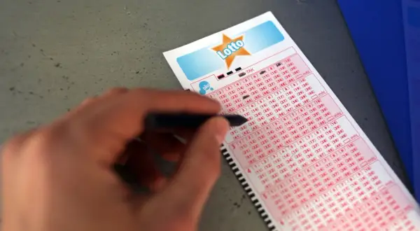 Ręka z długopisem zaznacza liczby na kuponie Duży Lotek. Dowiedz się, jak wypełnić kupon lotto duży lotek i spróbuj szczęścia!