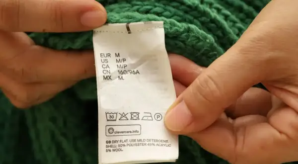 Etichetta di un maglione verde: non usare candeggina su poliestere. Asciugare in piano, usare un detergente delicato.