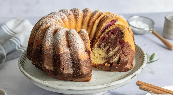 Ein saftiger Marmorkuchen mit Kirschen, bestäubt mit Puderzucker, auf einem rustikalen Kuchenständer.