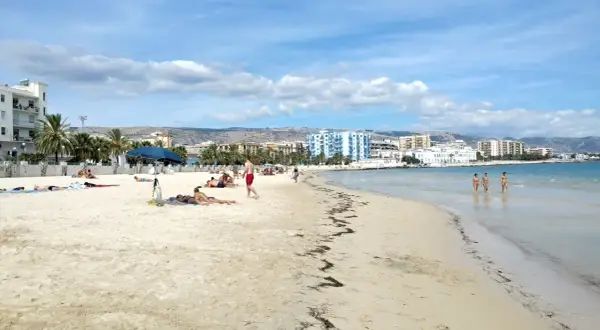 Spiaggia di Manfredonia con persone che prendono il sole e tre donne che camminano nell'acqua cristallina.