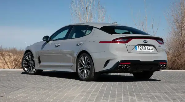 Kia Stinger GT CV gris, visto desde atrás, aparcado sobre adoquines grises.