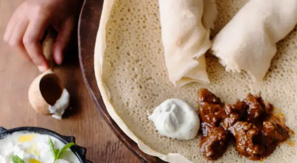 En hand tar en bit av en injera, en etiopisk rätt med kött och sås. Ett perfekt injera recept för en smakrik måltid.
