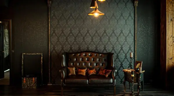 Elegancka skórzana kanapa i stolik tworzą przytulny kącik. Wnętrze w stylu vintage, z tapetą w ornamenty i stylowymi lampami, zaprasza do relaksu.