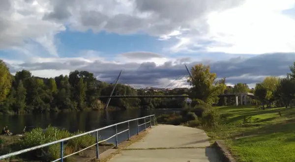 Paseo junto al río Miño, con el puente del Milenio y la playa fluvial de Ourense al fondo. Nubes amenazantes en el cielo.