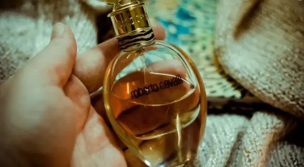 Dłoń trzyma elegancką buteleczkę perfum Roberto Cavalli EDP z płynem w kolorze bursztynu, ozdobioną złotym korkiem i wzorem w panterkę.