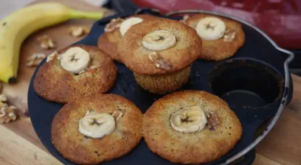Frisch gebackene Bananen Nuss Muffins, garniert mit Bananenscheiben und Walnüssen, liegen in einer Muffinform.