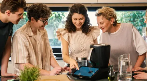 Pięć osób przygląda się ekranowi urządzenia kuchennego, szukając inspiracji na thermomix top 10 przepisów.