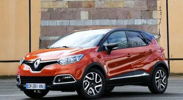 Pomarańczowy Renault Captur 2016 z czarnym dachem stoi przed ceglaną ścianą.