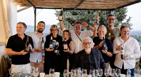 Un gruppo di persone sorridenti, alcuni con bottiglie di vino, celebra i papi marchigiani.