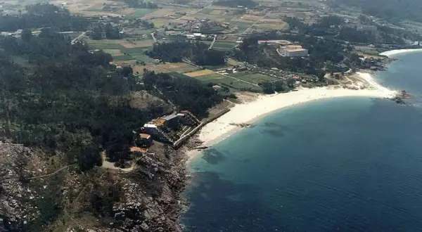 Vista aérea de la **playa de Cabeiro**, con arena blanca, aguas turquesas y un paisaje rural salpicado de casas y vegetación.