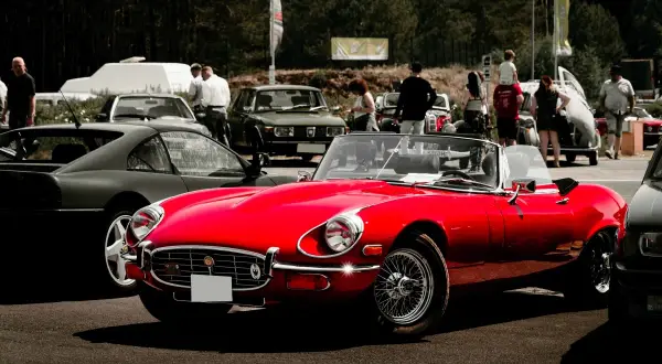 Roter Oldtimer-Cabriolet glänzt auf einem Treffen in Berlin. Im Hintergrund weitere Klassiker und Besucher.
