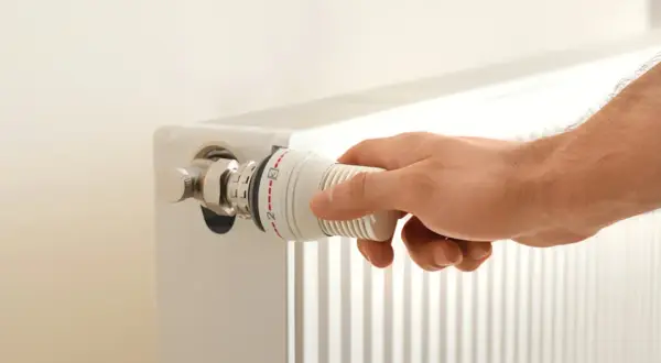 Hand dreht am Thermostatventil eines Heizkörpers. Die Markierungen zeigen eine Einstellung zwischen 2 und 3. Möglicherweise ist der Thermostat defekt.