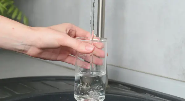 Main tenant une éprouvette graduée sous un robinet, on teste la qualité de l'eau pour s'assurer qu'elle respecte les normes TDS eau potable.