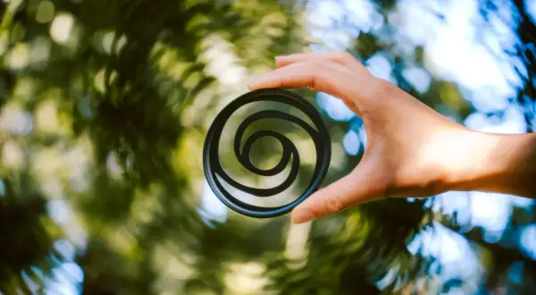 A hand holds a circular filter with a swirly bokeh pattern, creating a vortex of light and color.