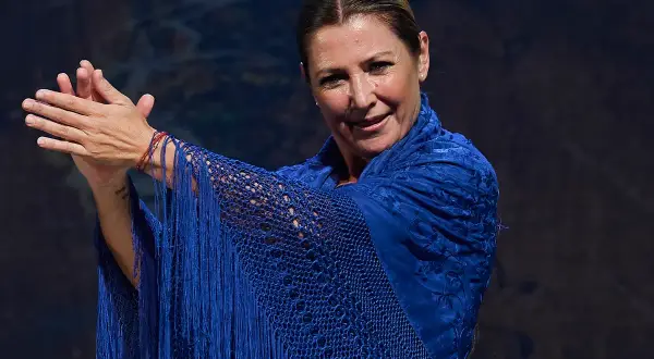Sara Baras, joven y vibrante, luce un mantón azul eléctrico con flecos, sus manos en un gesto flamenco.