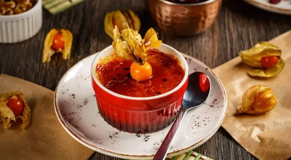 Słodka, karmelizowana crème brûlée w czerwonej kokilce, ozdobiona owocem miechunki.