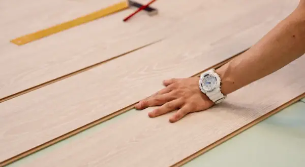 Mano con orologio bianco posata su pannelli di parquet chiaro, pronti per essere tagliati.