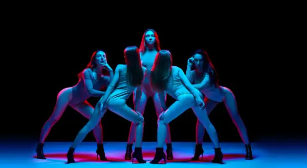 Pięć kobiet w body i butach na obcasach wykonuje zmysłowy taniec high heels w neonowym świetle.