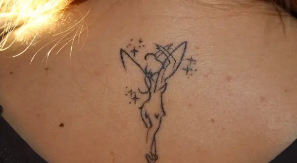 Delikatny tatuaż dzwoneczek z piotrusia pana na karku, otoczony magicznymi gwiazdkami.