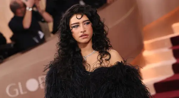 Odessa A'zion, con su cabello rizado y oscuro, luce un elegante vestido negro de plumas y un collar de diamantes.