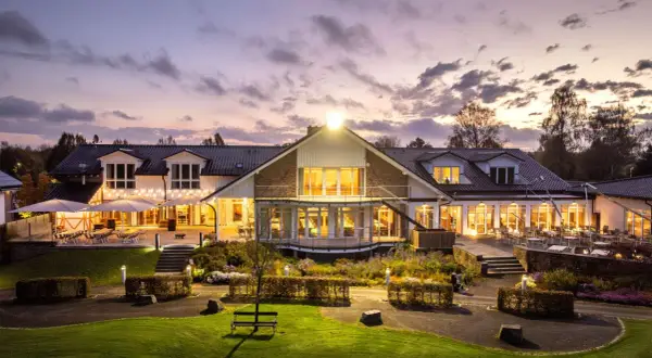 Abendstimmung am Golfclub Heckenhof. Beleuchtetes Clubhaus mit Terrassen und Gartenanlage im Dämmerlicht.