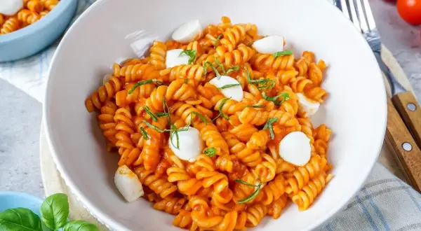 Eine Schüssel mit köstlicher One Pot Pasta, Fusilli in Tomatensauce mit Mozzarella-Kugeln und frischem Basilikum garniert.