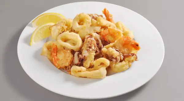 Un invitante piatto di frittura di pesce, con anelli di calamari dorati e gamberi croccanti, guarnito con spicchi di limone fresco.