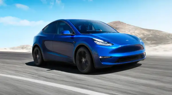 Blå Tesla Model Y kör på en väg i ökenlandskap. En dröm om en tesla till salu.