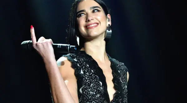 Uśmiechnięta Dua Lipa z mikrofonem w dłoni, podczas jednego ze swoich ekscytujących koncertów.