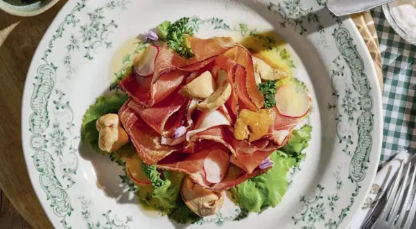 Deliziosi antipasti di terra con affettati rosa, funghi e verdure fresche su un piatto decorato.