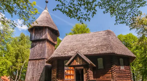 Drewniana cerkiew i dzwonnica na tle zieleni. To część największego skansenu w Polsce, gdzie można poczuć ducha dawnych czasów.
