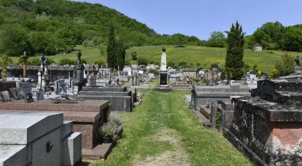 Vue d'un cimetière avec des tombes et des croix, sur fond de colline verdoyante.