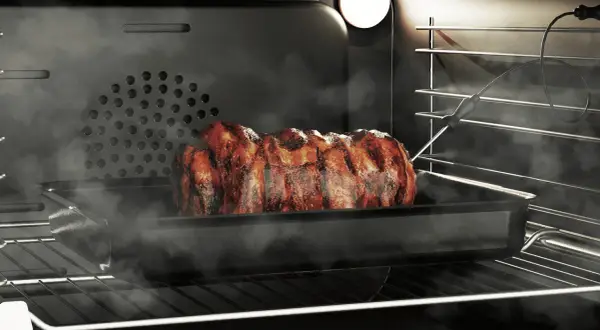 Soczysta pieczeń w piekarniku, wykorzystująca funkcję grill, paruje i apetycznie się rumieni.