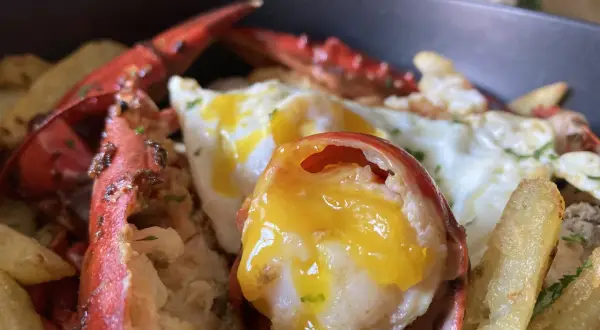Deliciosos huevos rotos con bogavante, patatas fritas crujientes y un huevo con la yema perfecta.