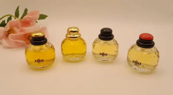 Cztery miniaturowe flakoniki perfum YSL Paris, obok delikatnych różowych kwiatów.