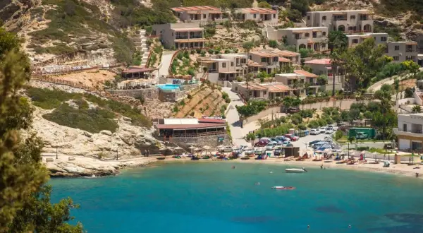 Widok na zatokę z turkusową wodą, plażą, budynkami hotelowymi na wzgórzu i basenem.