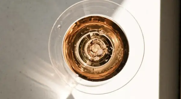 Szklanka z różowym, musującym winem dealkoholizowanym, w świetle słońca. Bąbelki unoszą się ku górze.