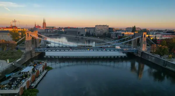 Most wiszący nad Odrą rzeką jak płynie, z widokiem na miasto i katedrę.