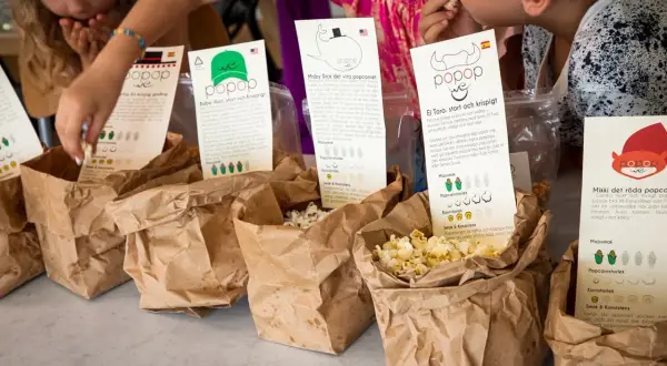 Barn plockar popcorn ur papperspåsar. En påse med popcorn med kolasås syns tydligt.