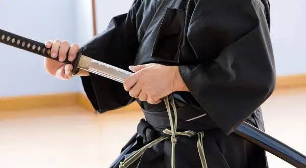 En person i svart dräkt håller ett samurajsvärd, en symbol för japanska krigare.