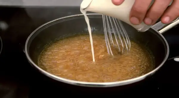 Se añade líquido a una sartén con salsa burbujeante, usando un batidor para espesar salsa con maicena.