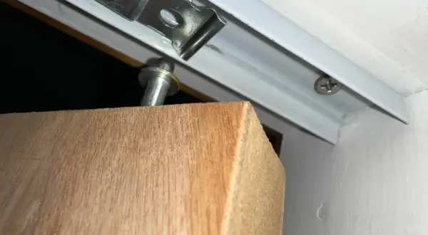 Detalle de una puerta armario descolgada, con el soporte metálico visible y el borde de madera.