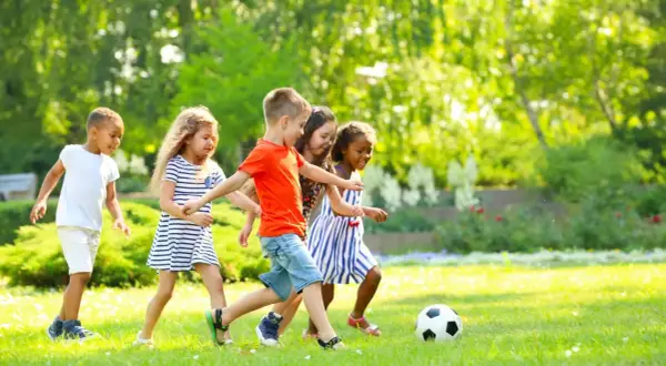 Kinder haben Spaß bei Bewegungsspielen im Kindergarten. Sie spielen Fußball auf einer sonnigen Wiese.