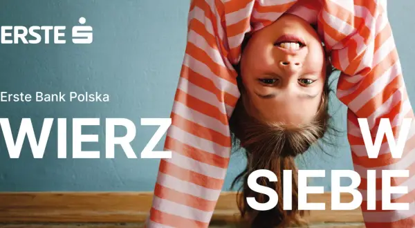 Uśmiechnięta dziewczynka w pasiastej bluzce robi mostek. Logo Erste Group i hasło "WIERZ W SIEBIE" zachęcają do wiary we własne możliwości.