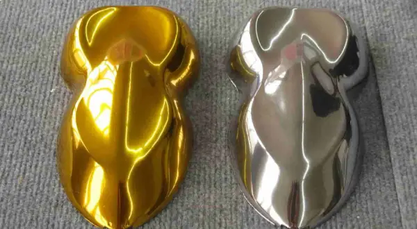Due campioni di vernice, uno oro brillante e l'altro con un effetto cromo colore metallico, riflettono la luce su una superficie grigia.