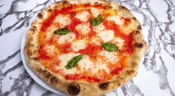 Pyszne ciasto na pizzę neapolitańską, z sosem pomidorowym, mozzarellą i bazylią, idealne na letni wieczór.
