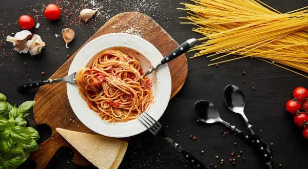 Talerz spaghetti z sosem pomidorowym, czosnek, pomidory, bazylia i parmezan. Takie składniki sugerują, skąd pochodzi spaghetti.