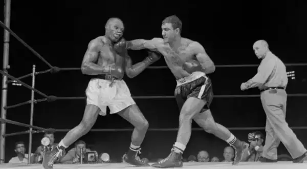 Two boxers in a ring, one landing a punch. The boxer on the right, with a powerful Rocky Marciano physique, is throwing a jab.