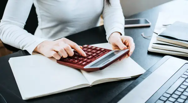 Kobieta liczy wydatki na własne cele mieszkaniowe, przygotowując PIT-39. Na biurku notatnik, kalkulator i laptop.