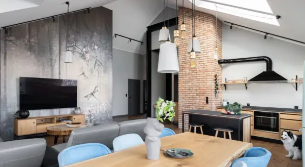 Nowoczesny styl loftowy salon z jadalnią i kuchnią. Ściana z motywem ważek, szara sofa, drewniany stół i ceglana ściana.